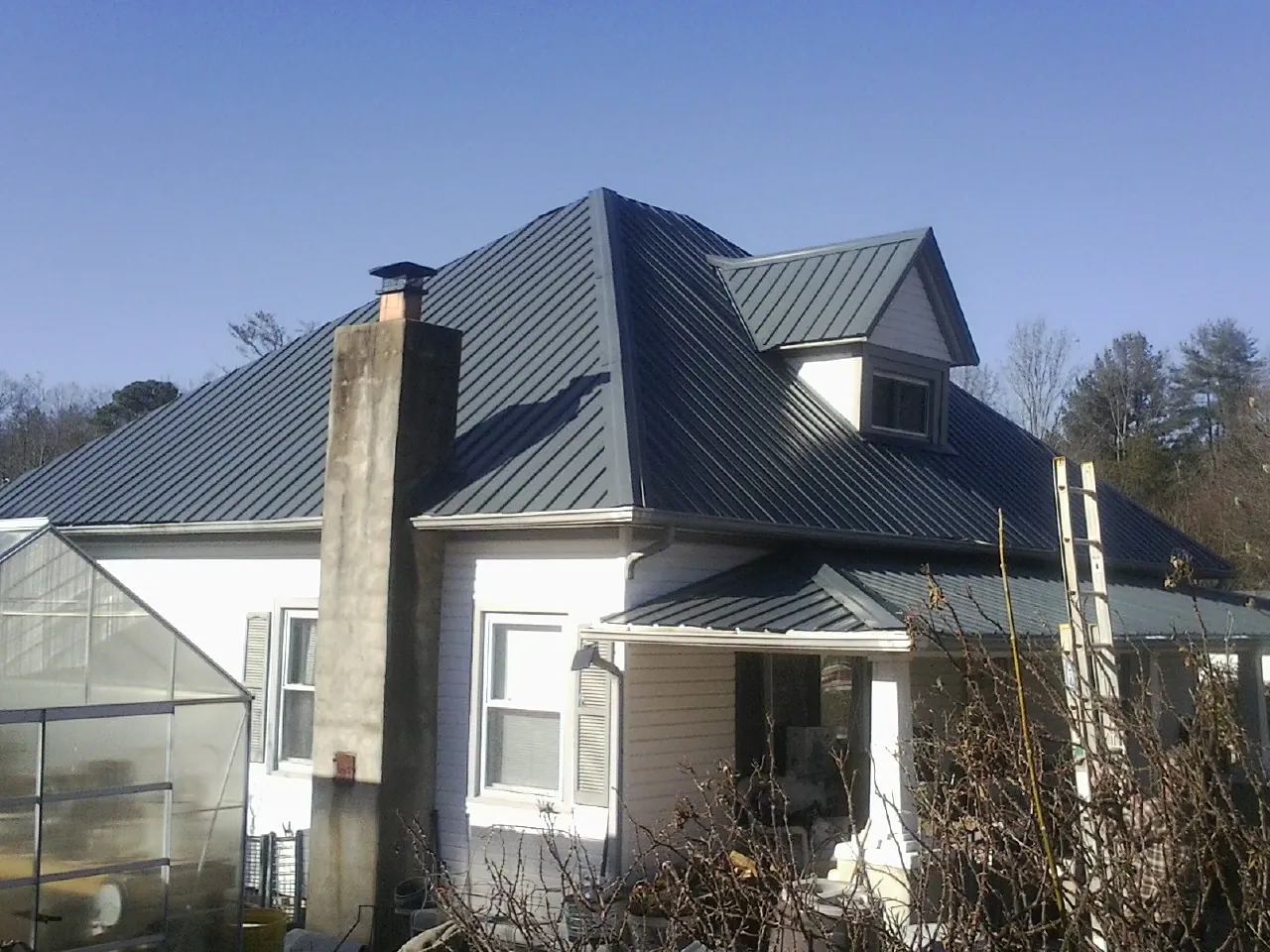 Dark blue standing seam metal roof on a white farmhouse with dormer — Slate & Tile Roof Repair by Roofing Brothers in Goffstown