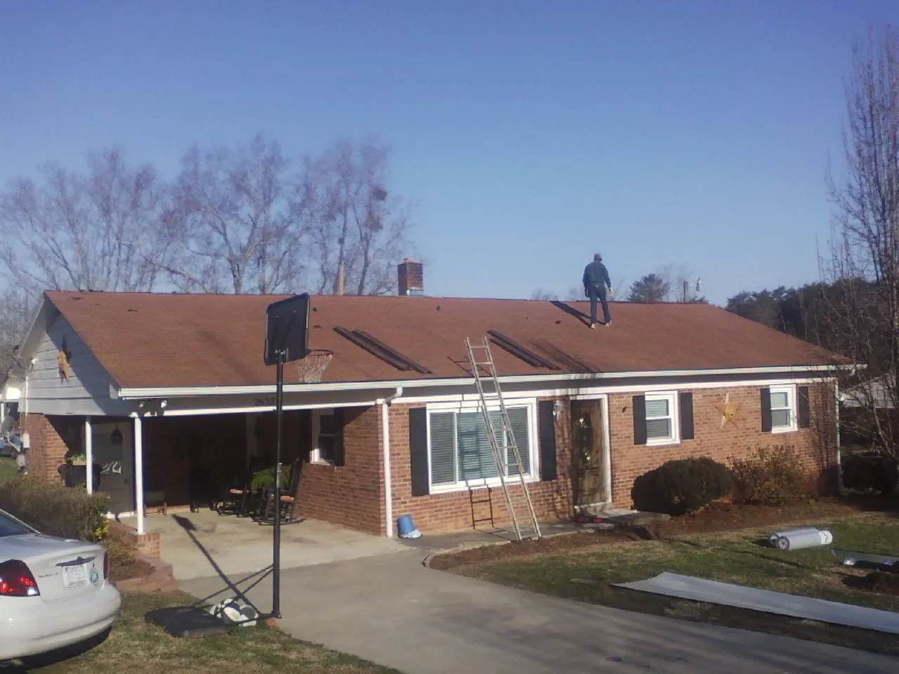 Roofer stripping a shingle roof on a brick ranch before metal panels in Goffstown