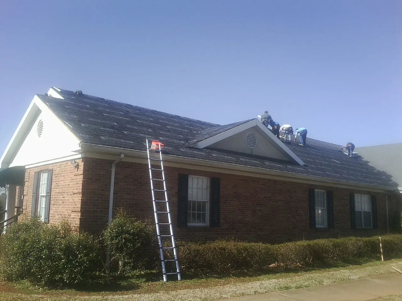 Crew tearing shingles off a brick ranch roof with a ladder set — Emergency Roof Repair work by our crew in Goffstown