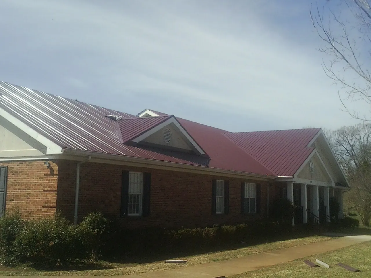 Red metal roof with gabled entries on a long brick building, from a Hail Damage Roof Repair job in Goffstown