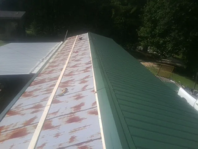 Old rusted panels beside newly installed green metal roofing — Wind Damage Roof Repair by Roofing Brothers in Goffstown
