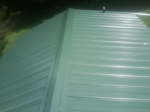 New green metal panels meeting at the ridge of a roof — Flat Roof Repair work by our crew in Goffstown