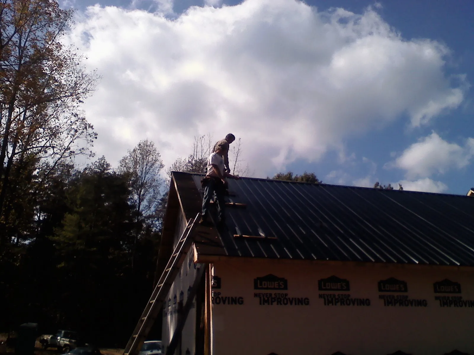 Roofer fastening dark metal panels high against a cloudy sky, from a Roof Inspection job in Goffstown
