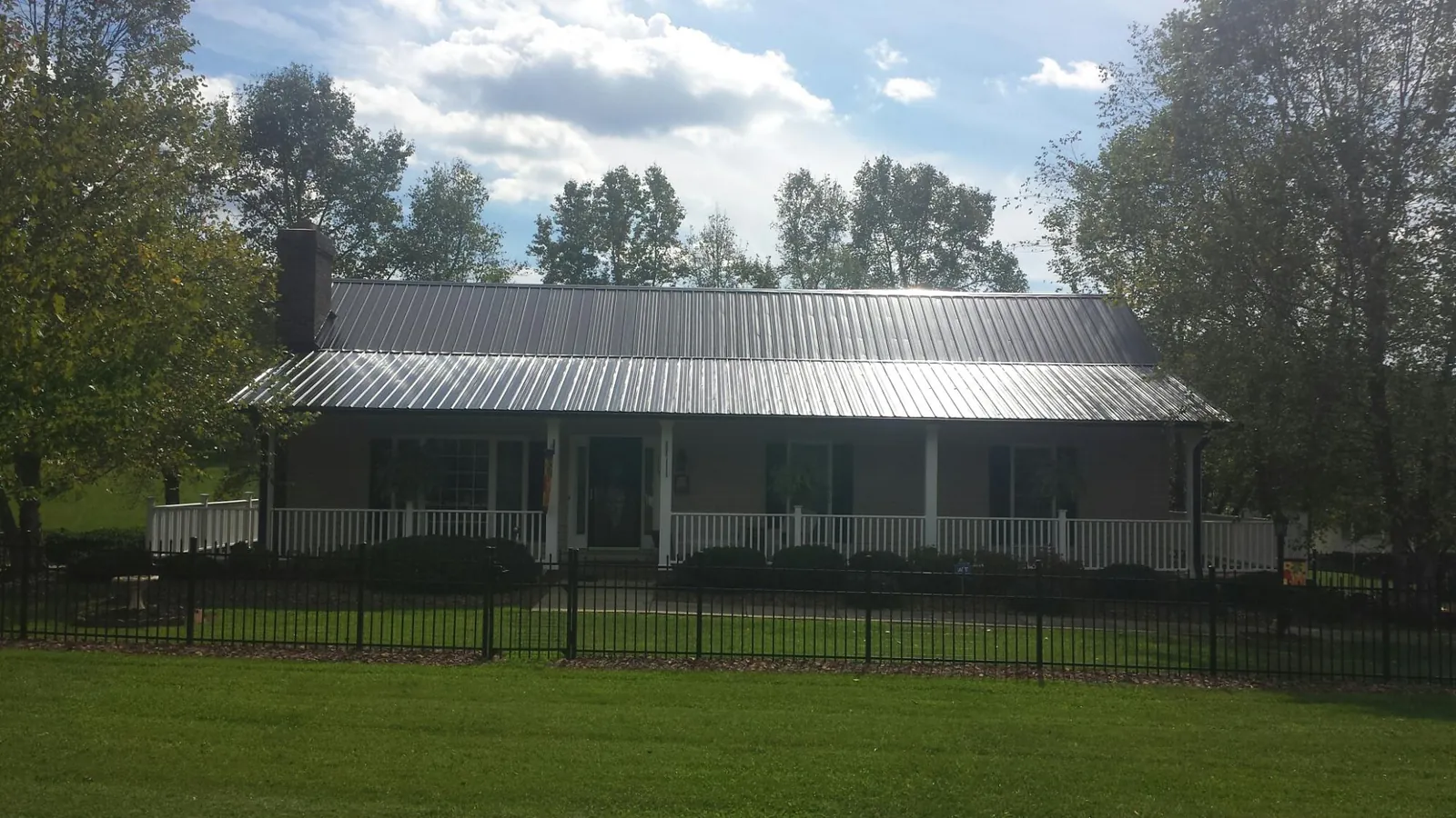 Gray metal roof on a brick ranch with a full width front porch — Gutter Guard Installation work by our crew in Goffstown