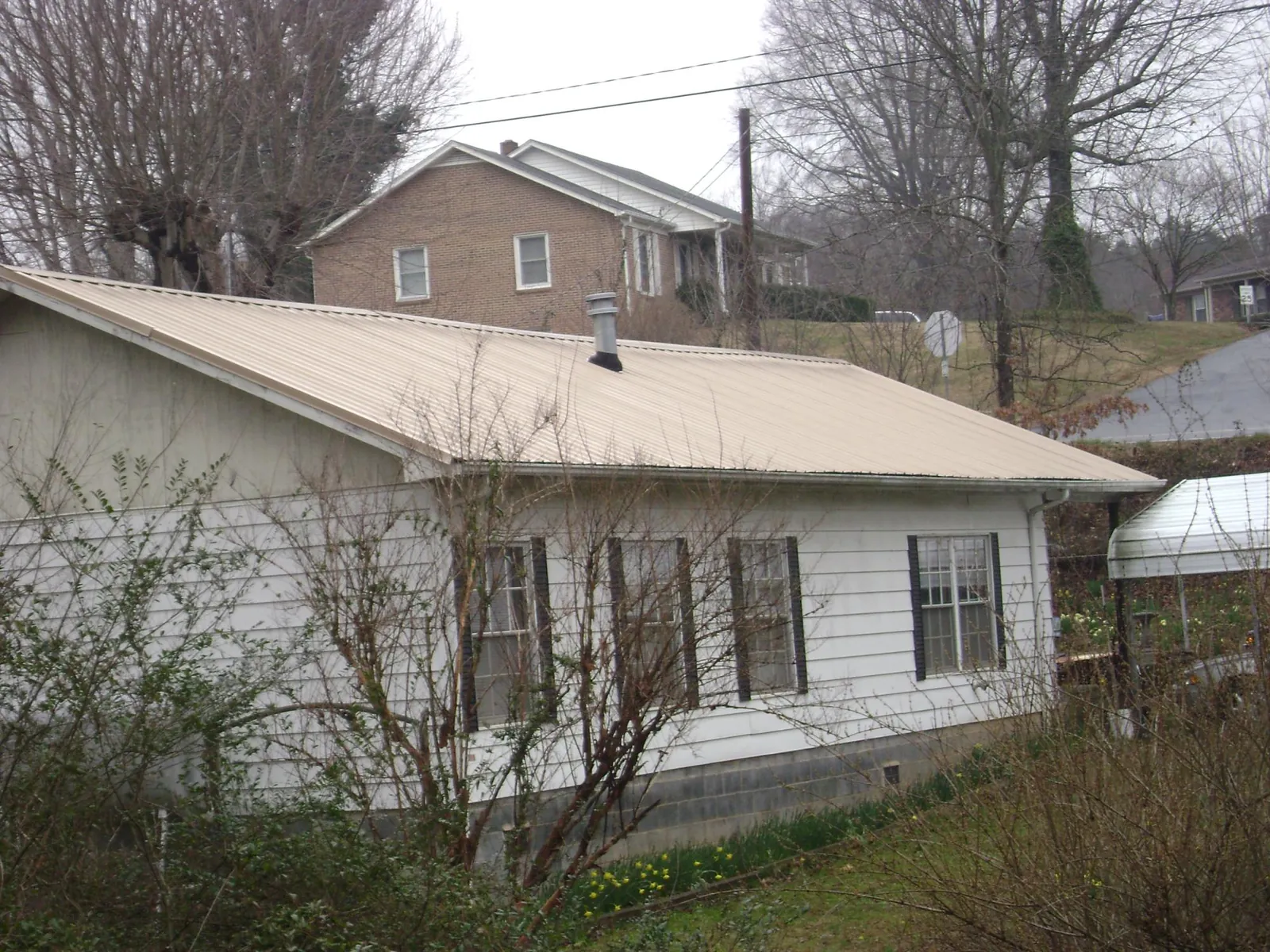 Tan metal roof on a white sided house set into a hillside — Commercial Roofing by Roofing Brothers in Goffstown