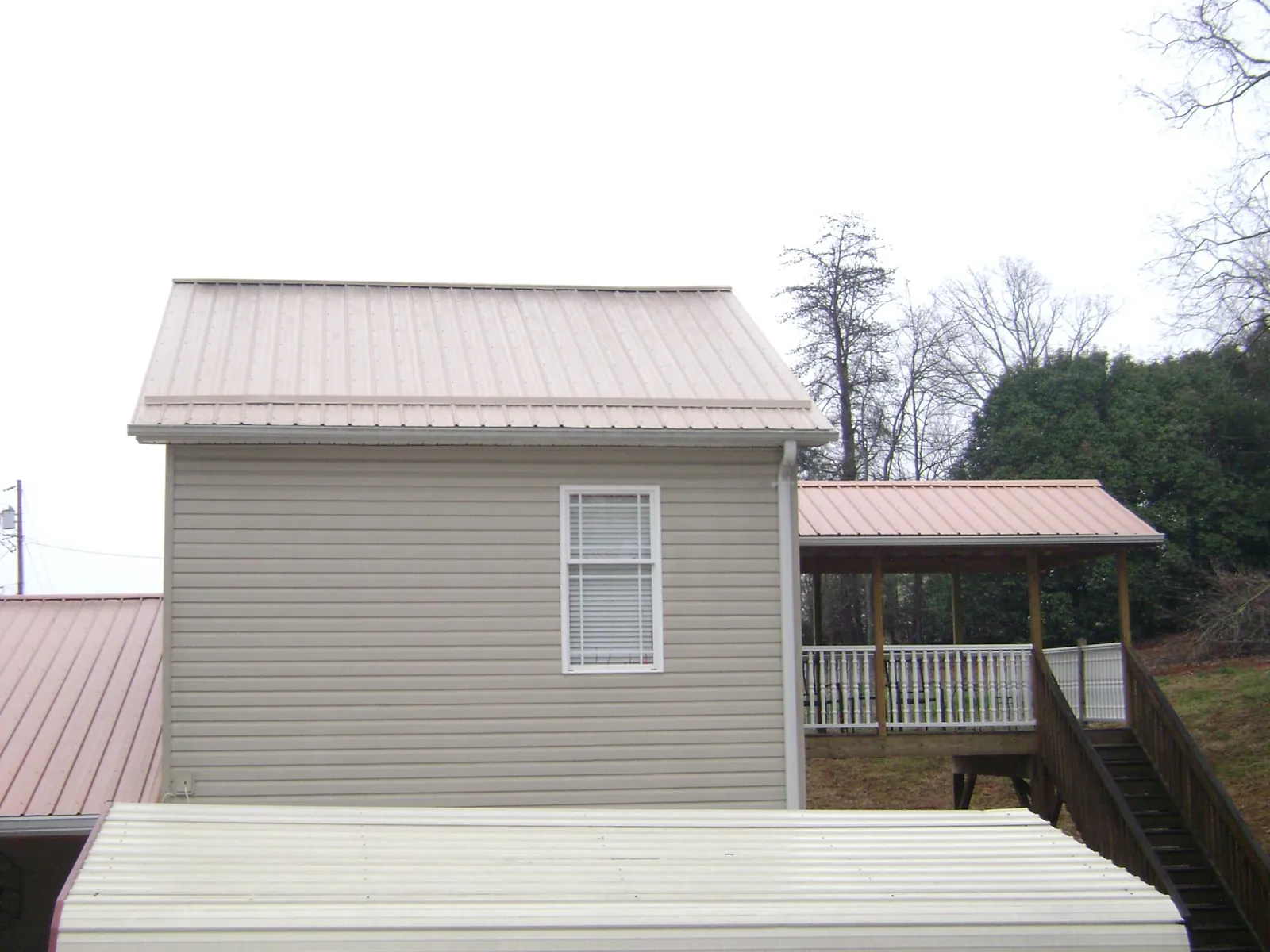 Tan metal roofs on a two story addition and attached porch, from a Roof Replacement job in Goffstown